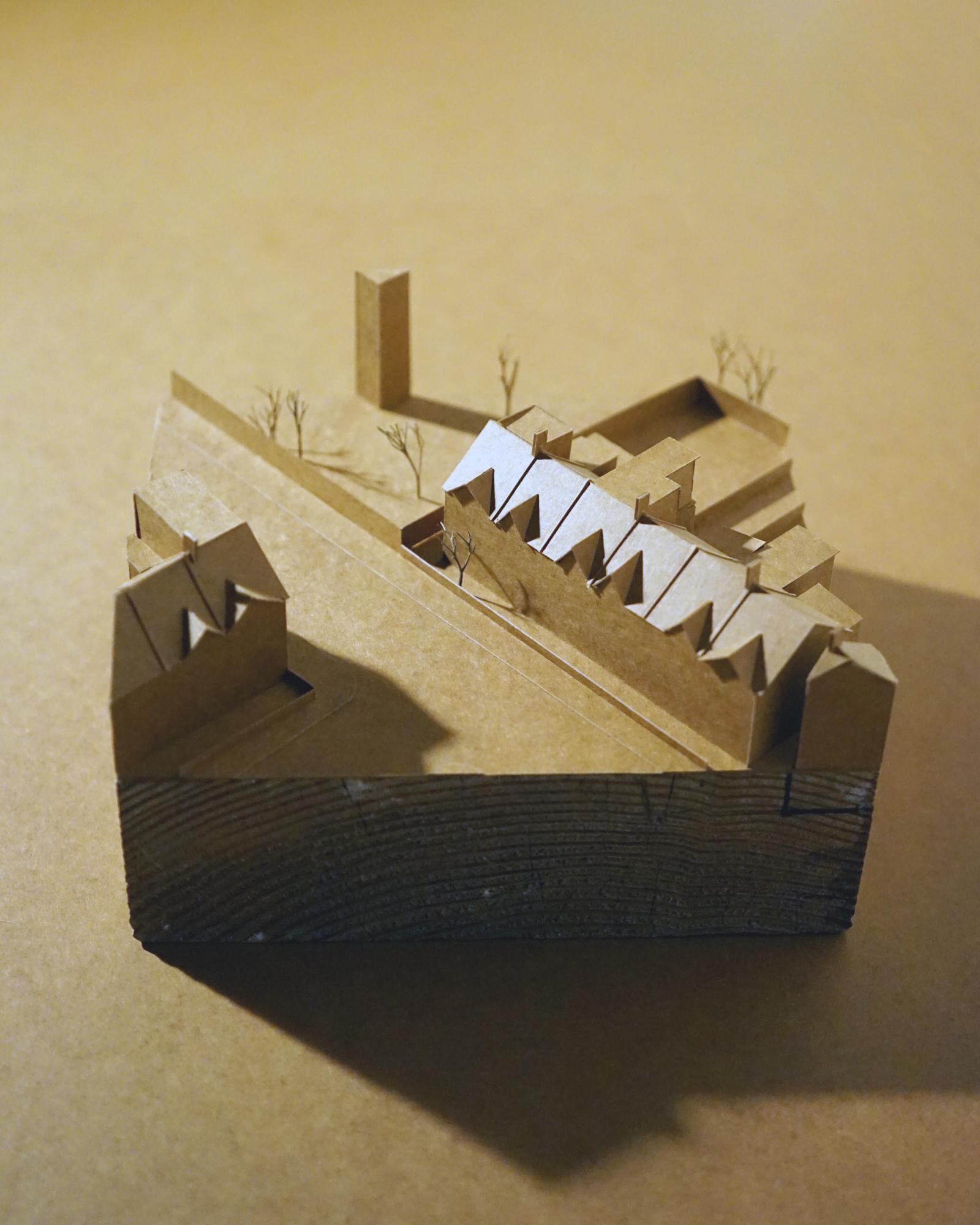 House for Astrid and Freddie, 1.200, Neighbourhood Model
This model was made to situate the proposed house within its immediate urban context and to test its relationship to the existing fabric. Working at 1:200 allowed the scale, roof forms and collective rhythm of the street to be understood as a whole, rather than as a backdrop.

The model was used to explore how the building's adaptations participate in the shared life of the neighbourhood. Massing, height and roof geometry were adjusted to test conversations with adjoining buildings, the handling of corners, and the way the proposal mediates between public impression and private interior. The ground is modelled as a continuous surface, reinforcing the idea of the house as part of a larger terrain shaped by use, movement and history.

For the viewer, the model clarifies the proposal at the end of a terrace as a contextual act rather than an isolated object. It shows how the design is shaped by adjacency, scale and collective form, and how modest shifts in volume and profile can have wider spatial and social effects. The model foregrounds neighbourhood as an active design condition, where responsibility to the street and its inhabitants informs architectural decision-making.
Handmade in card and timber off-cut from construction
Benjamin Machin and Lewis Foster-Jeapes, Architectural Assistant