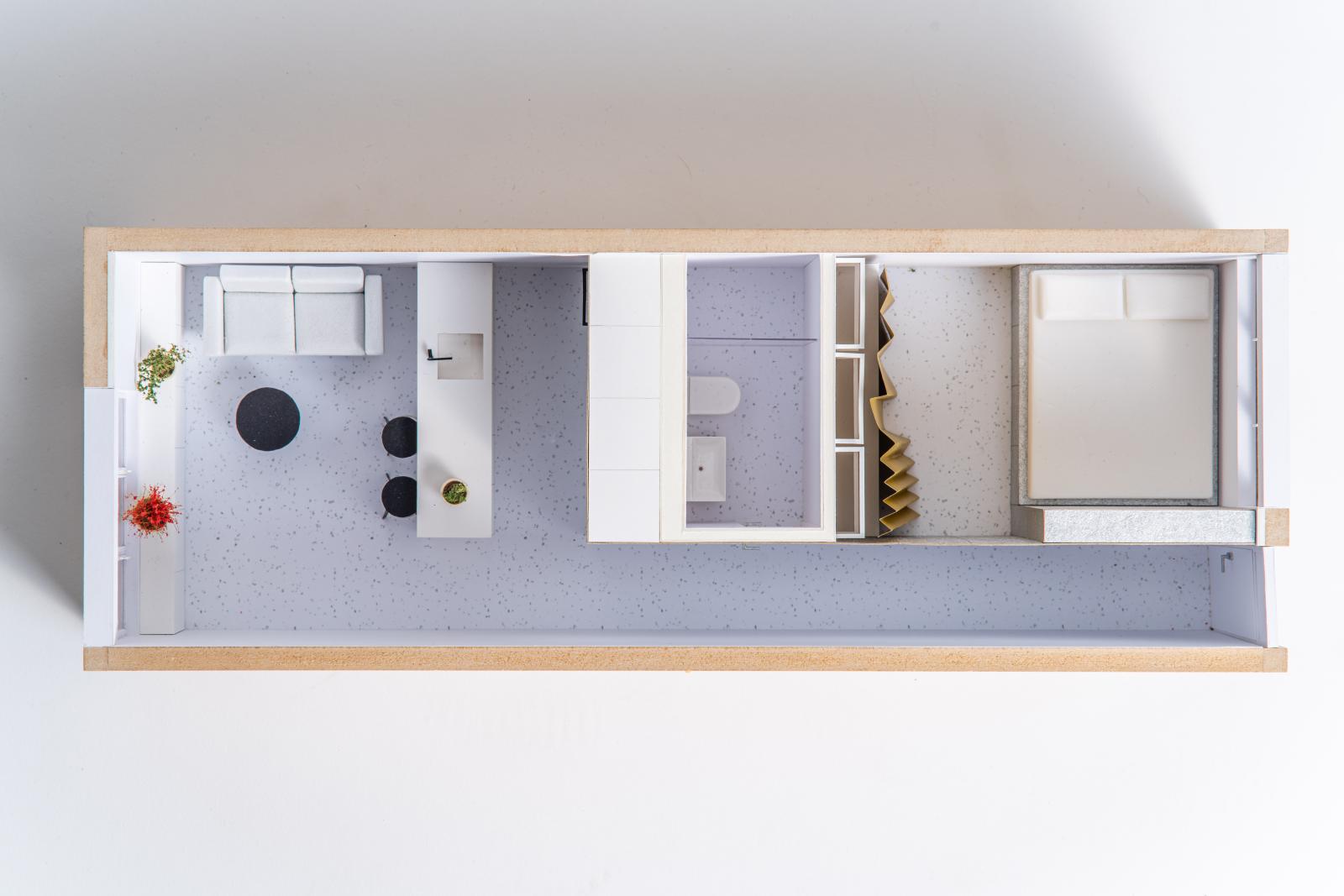 Micro apartment Vukovarska, 1:25, apartment interior model


This model illustrates the spatial transformation of a 31 m2 studio into a functional home for a family of three. Its primary purpose was to study the "compression" of functions, where the bedroom, bathroom, and service areas are condensed into a central, geometrically clear core to maintain an open living environment. We used the model as an iterative tool to resolve the apartment’s north-south organizational logic. By physicalizing the bespoke carpentry unit and the open-plan living area, we could test how daylight—enhanced by white surfaces and the speckled, semi-reflective floor—travels deep into the narrow floor plan. The model allows for a tactile exploration of the "blue box" strategy and the flexible boundaries created by elements like the pleated gold partition, which provides privacy without the weight of a solid wall. Ultimately, the model informs the viewer about the potential of high-density, precise design. It demonstrates how a single, integrated volume can organize a "bright box" for living, maximizing every centimeter while ensuring the space remains comfortable and uncluttered. It serves as a miniature "machine for living" that balances utility with a clear, minimalist aesthetic.

Wood, paper, Dry plants, foam, Kapa graph

Made by Superhands - Nikola Brlek