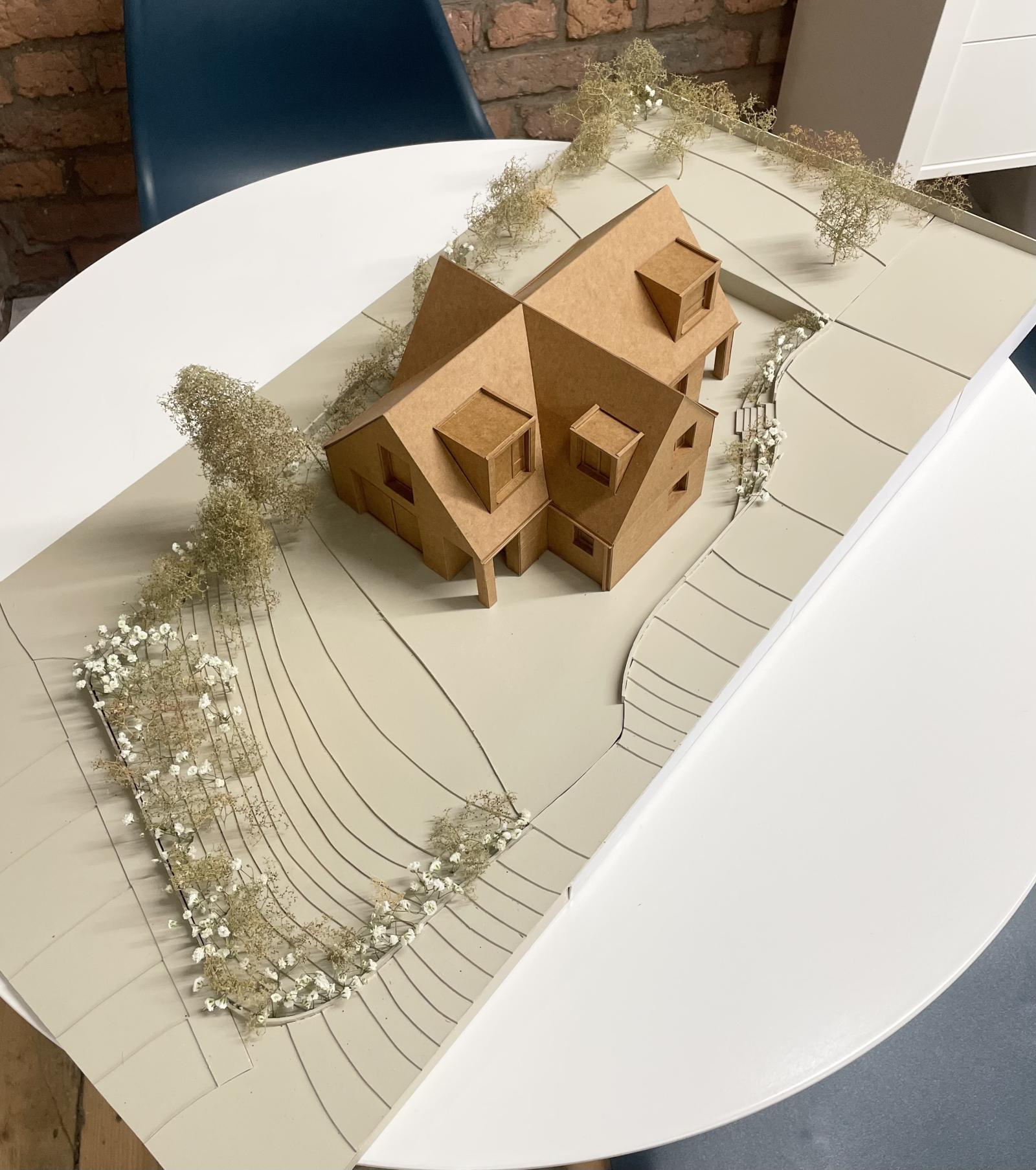 Holly Cottage. Scale 1:50. Building model

This model was used in the Design and Access Statement as well as for social media as the use of a single material for the building beautifully highlighted its unique form. By modelling the immediate surrounding site, it also allowed us to understand how the proposal sits within its landscape.

The use of one single colour of the waxed card subtly emphasises the window reveals, dormers, and overhangs of the design. As a more detailed 1:50 model, the project’s distinctive dual-axis form becomes clearly apparent.

Mountboard, waxed card, sea foam trees, gypsophila 

Made by Camila Alvarado, Part 2 Architectural assistant 