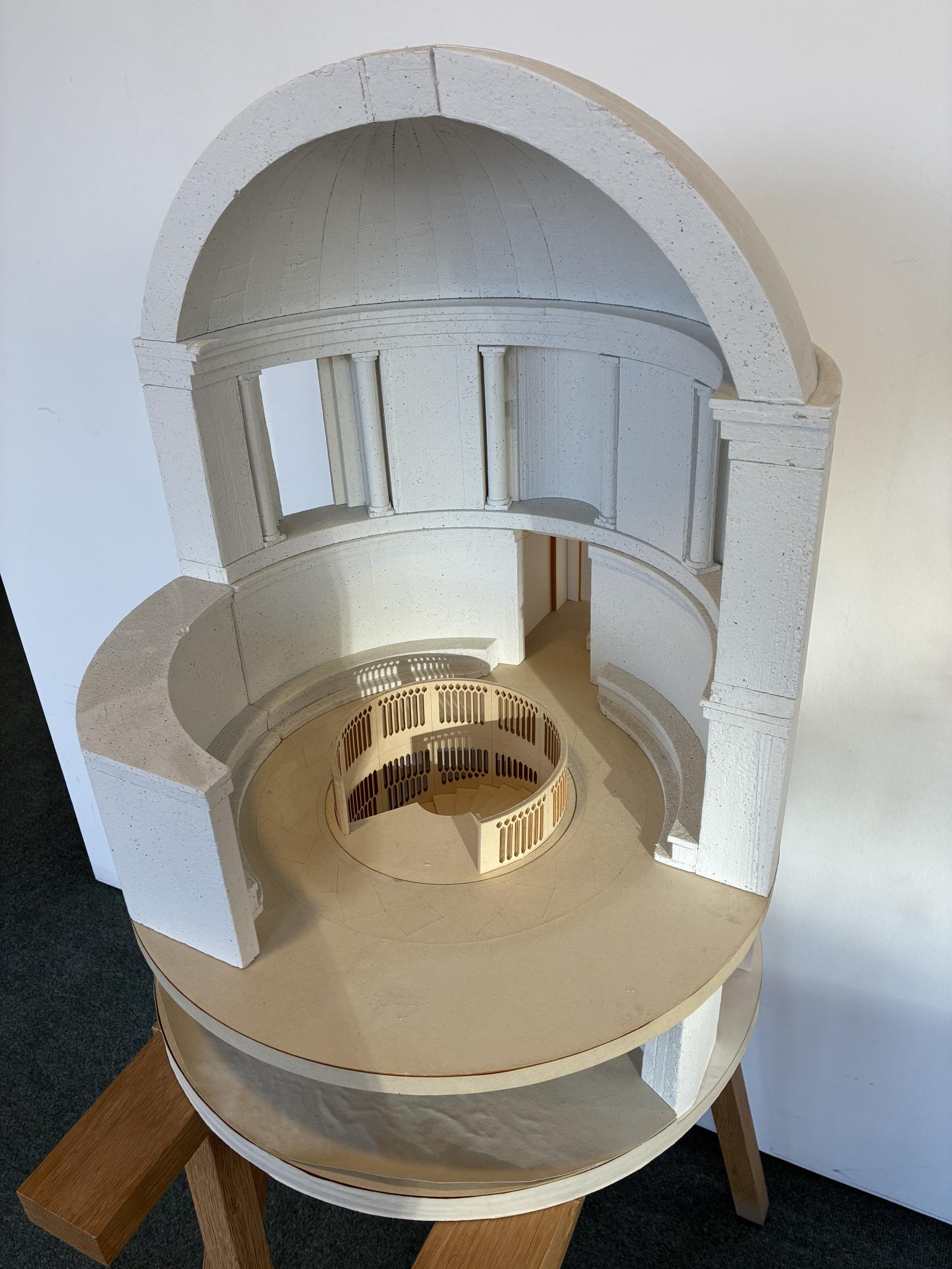 Rhodes House, University of Oxford, 1:25, Rotunda Stair

This study model investigates the design and construction of a new sculptural staircase within the historically significant Rotunda at the Grade II* Listed Rhodes House. While the Rotunda is an important memorial space, the intervention provides a subtle yet contemporary response to the existing stonework.

Made by a member of the design team, the model was used primarily to test stair details and construction strategies, exploring proportions, structure, and how the new stone stair could be realised within the existing fabric. Its form responds to Herbert Baker’s architecture, balancing solidity and openness while maintaining light, views, and the Rotunda’s integrity.

This is a typical sketch model that we might make, constructed quickly from polystyrene, card, and foamboard. It allowed the team to experiment with multiple options. The iteration shown here captures the final design of this significant intervention.

Model Making Team

Cameron Frame
Stephen Setford

Design Team

Paul Williams
Stephen Hadley
Tom Fotheringham
Jason White
Cameron Frame

Polystyrene, Paint, Foamboard, Card, Paper