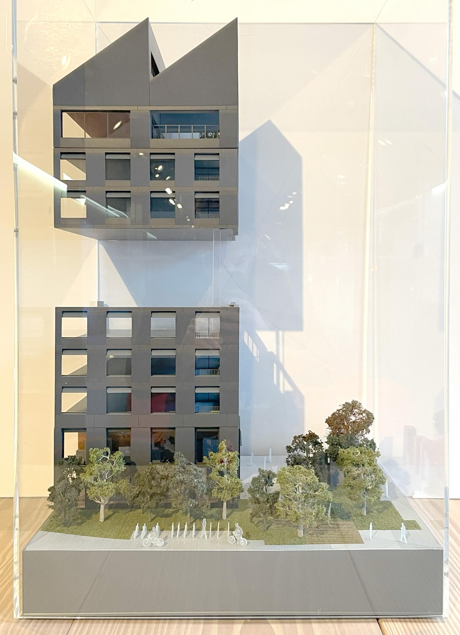Sister C2 - Corner Bay Study Model / 1:75 / Facade Model

Certain building corners are framed and expressed throughout Sister Plot C. These moments are emphasised by the offset plan diagram of the two buildings and their relationship to the surrounding context. The model focuses on the north-eastern corner of Sister C2, demonstrating how several defining characteristics of the scheme are present in a single vertical composition. It presents how the building engages with the public realm at ground level and contributes to wider city views at roof level.

The model represents the visual connections between the community space of the Manchester Room and the public realm, framed by robust precast piers whose tone and texture are informed by the board-marked Hollaway Wall. Articulated external amenity spaces provide breakout areas to each office floor, introducing shadow and depth to the elevation. This vertical composition culminates in a distinctive single bay at roof level, forming part of the building’s sawtooth silhouette and marking its presence on the skyline.

SLA 3D print, Laser cut acrylic, Spray applied paint finish

Gareth Verbiest - Modelmaker, Heather Whitehead - Modelmaker, David Euinton - Architect, Chris Trundle - Architect