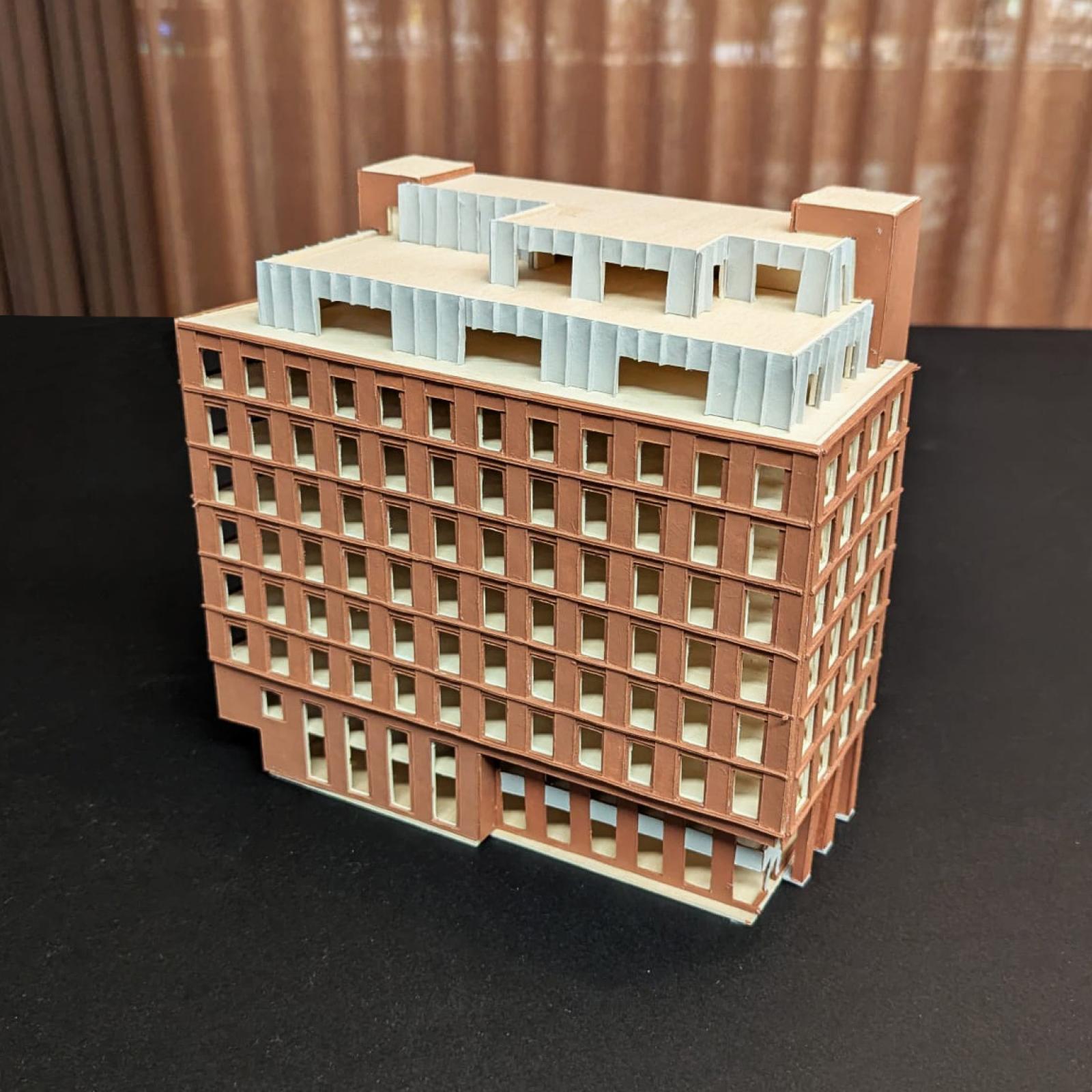 35 Fountain Street, 1:200, Facade and Massing Study

This 1:200 card model communicates the overall massing and scale of the proposed design for 35 Fountain Street, a low-carbon retrofit of an early 2000’s office building within Manchester’s central business district. The model tests the relationship between the retained structure and a proposed extension using a hybrid CLT and steel construction, enabling the proportions of the new façade that clads the existing steel frame to be studied and refined. 

At this scale, the model presents sufficient detail to test the articulation and rhythm of the façade while providing a clear representation of the building’s overall form and composition across all elevations. The nature of card focuses attention on form, proportion and spatial hierarchy, allowing an investigation of solids and voids and revealing key relationships such as roof setbacks, floor-to-floor heights and orientation. 

Laser-cut Card

Made by Katy Webb, Architectural Assistant & Sam Gills, Associate